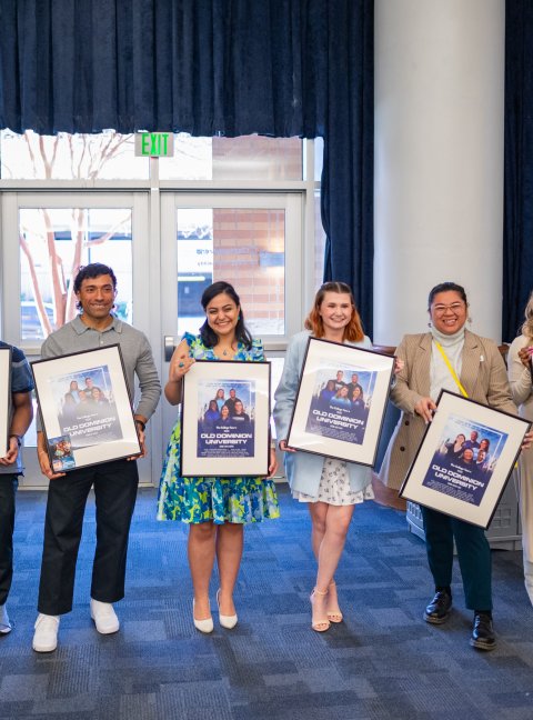 students standing while each holding a framed movie poster