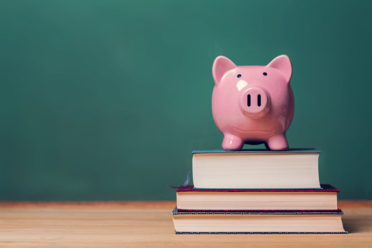 Piggy bank on top of books with chalkboard, cost of education theme