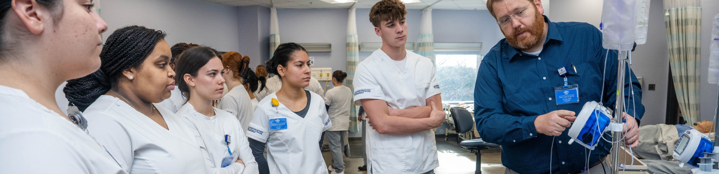 Nursing students in medical simulation lab watch instructor use medical device.
