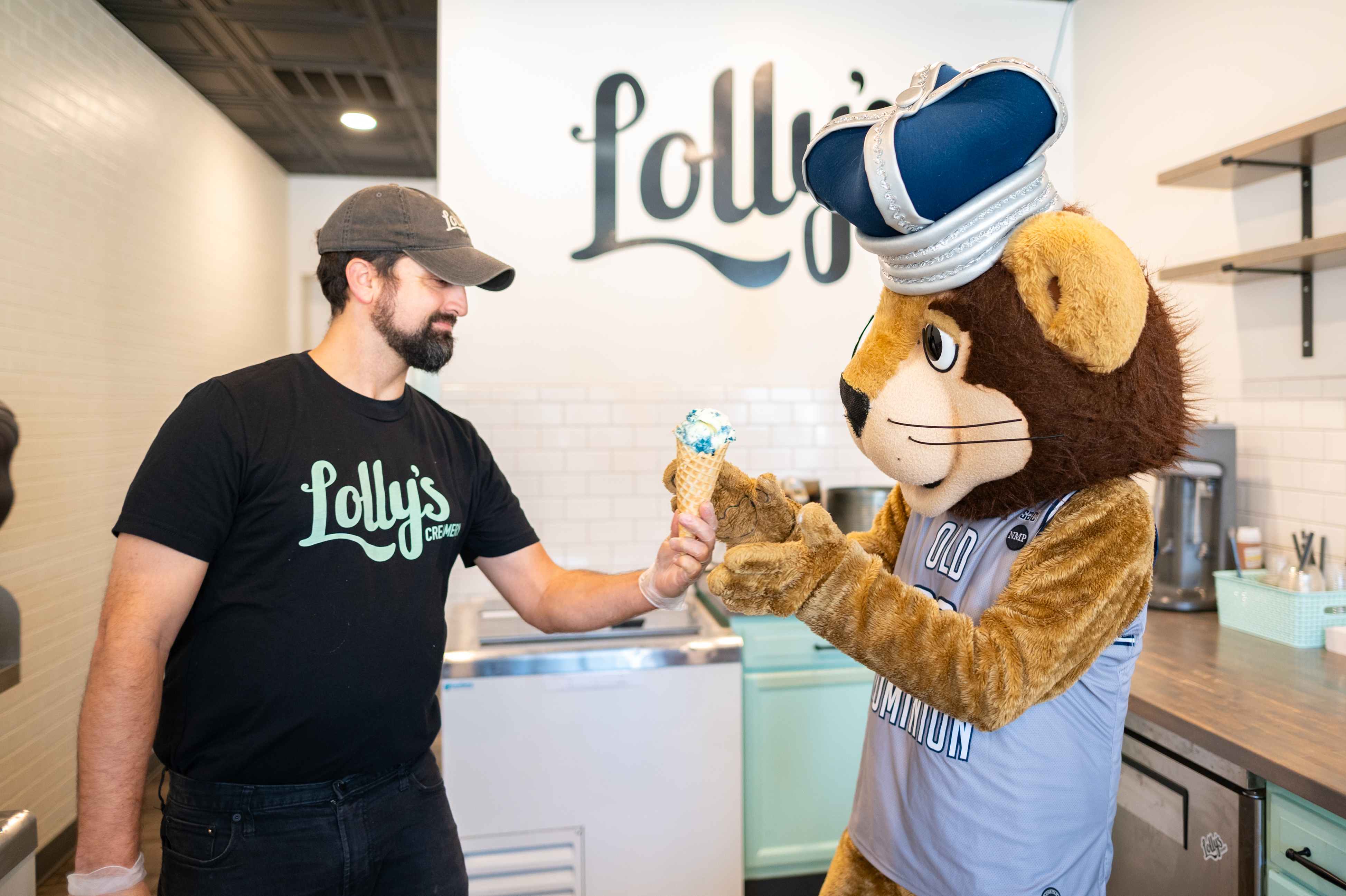 A man hands ice cream to a lion mascot.