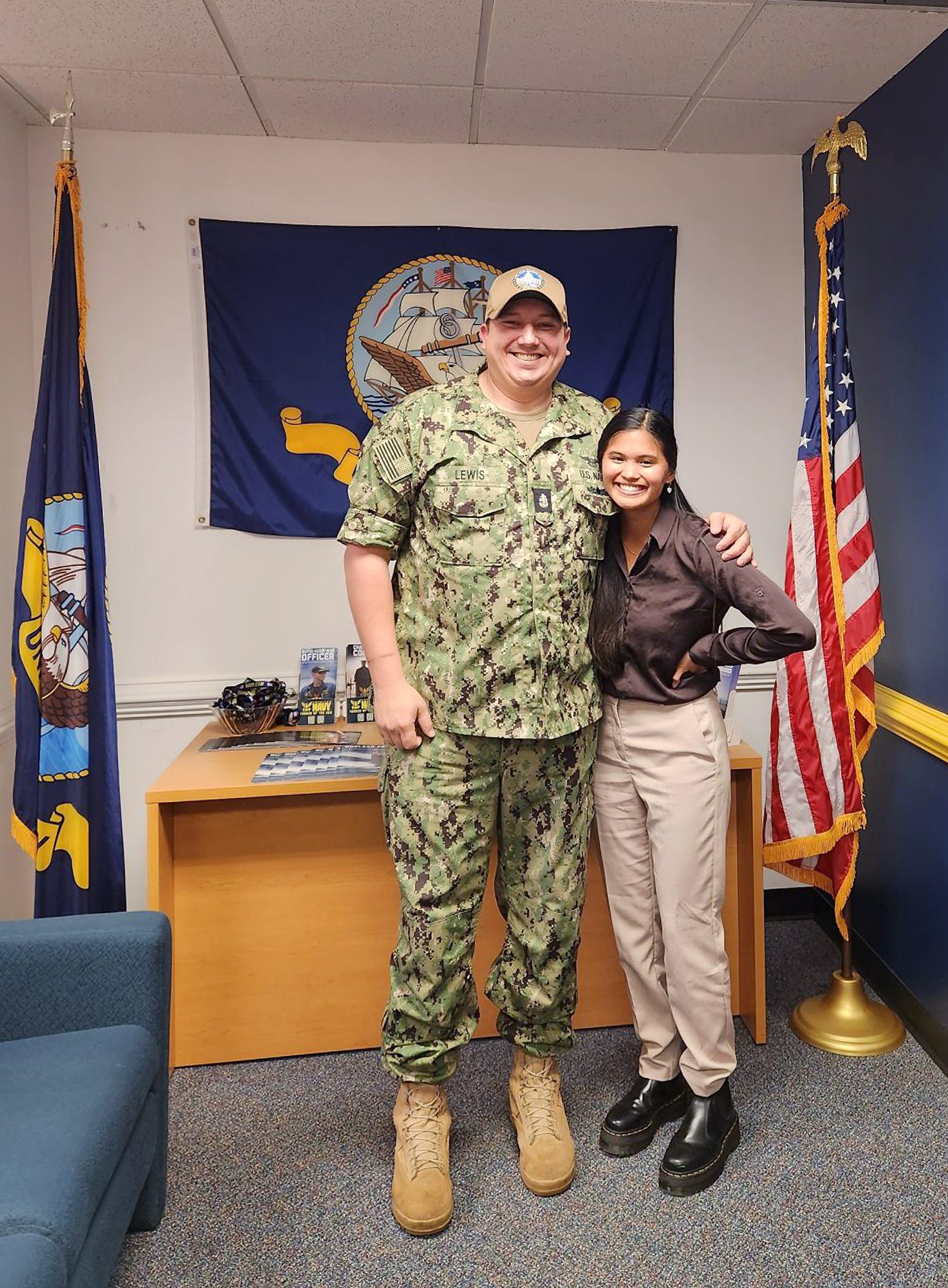 Tall man in a military uniform stands with woman in recruiting office