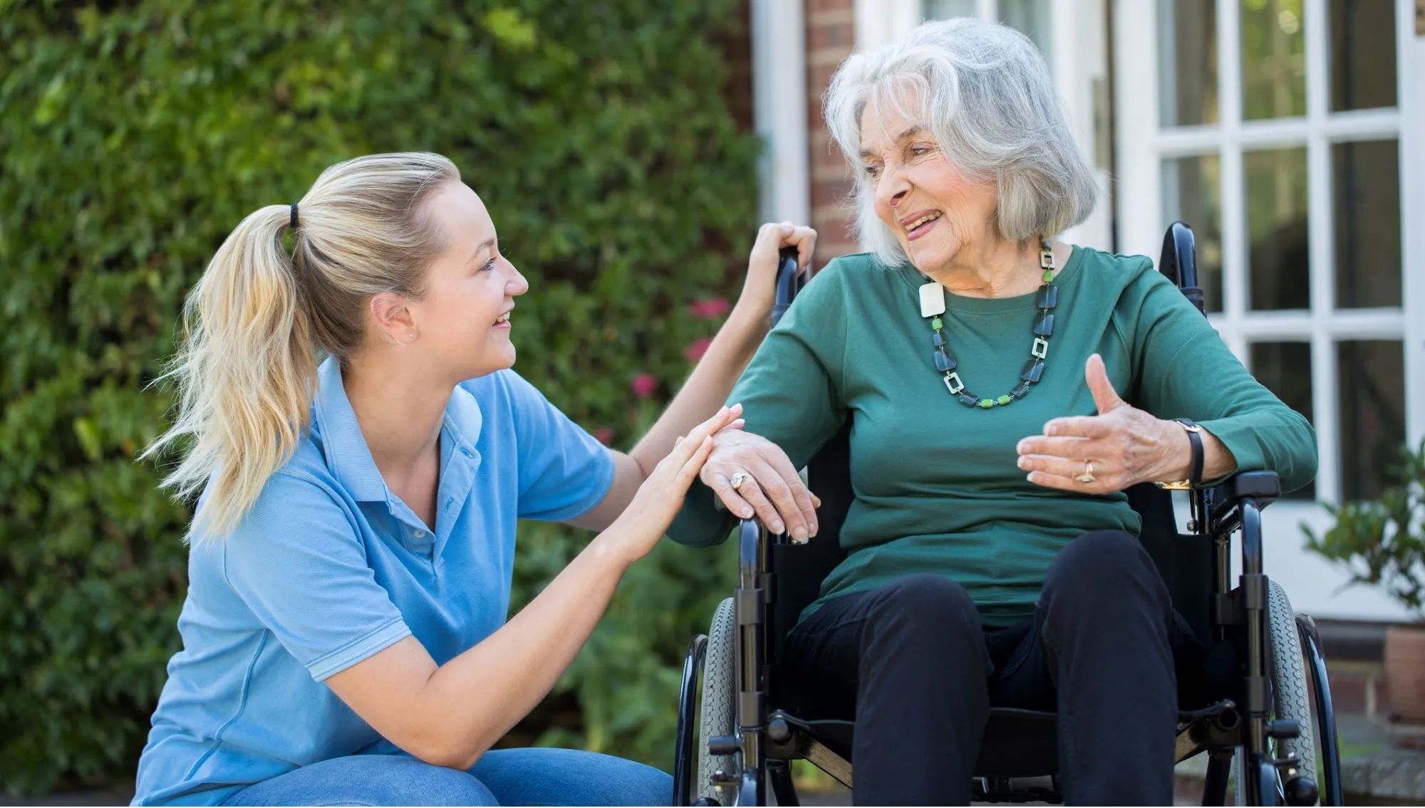 Nurse crouching by lady in wheelchair