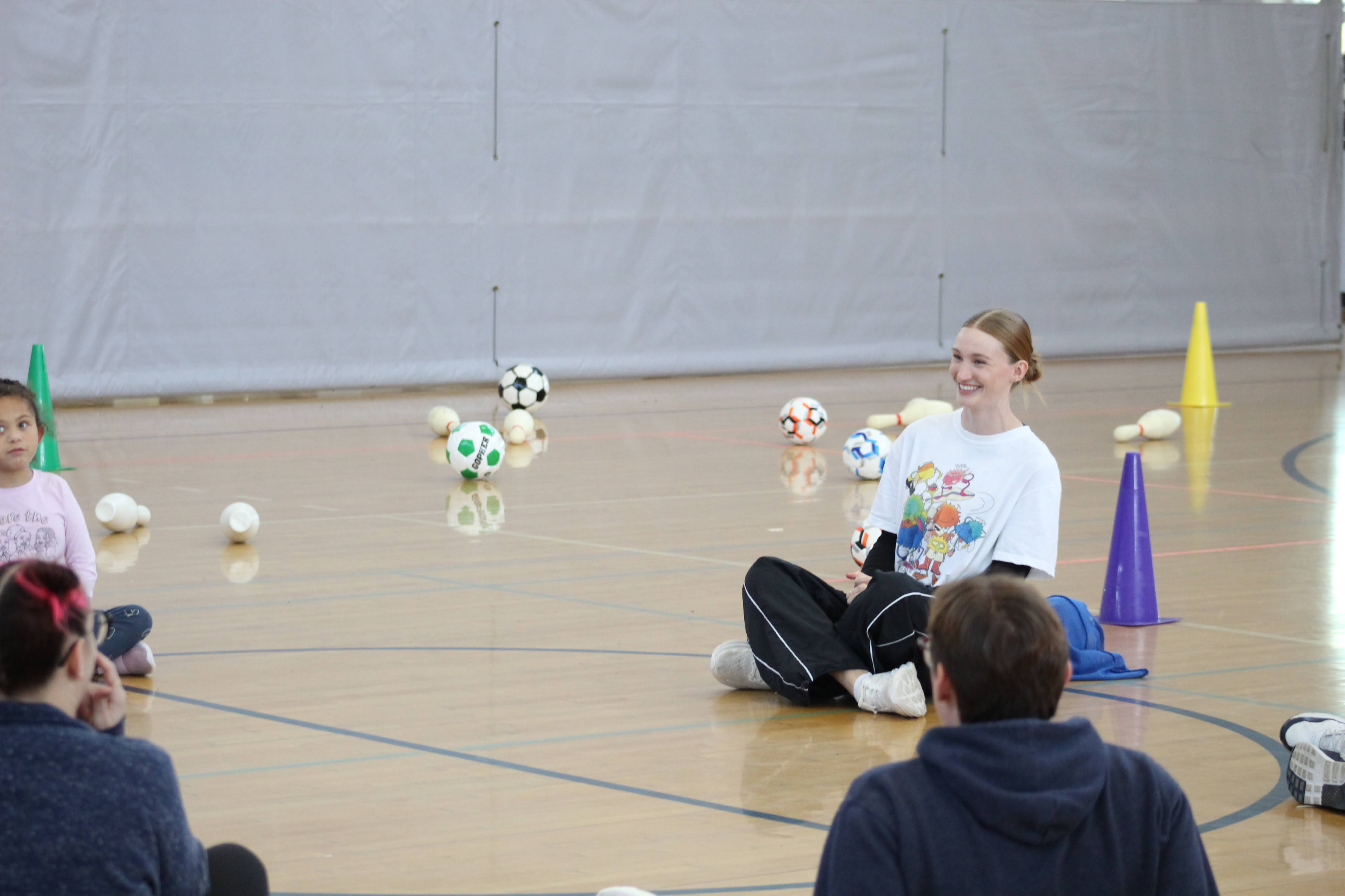 Baillie Ollila sits on gymnasium floor along with four other people.