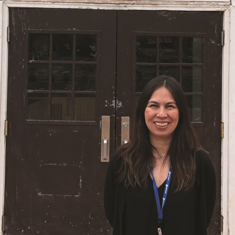 A woman stands smiling in front of a brick building.