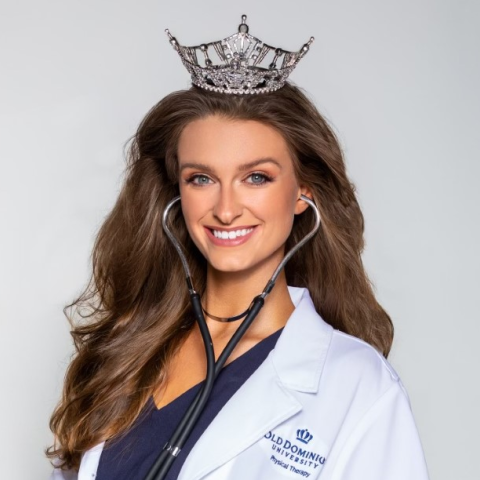 A woman poses wearing a lab coat and a crown.