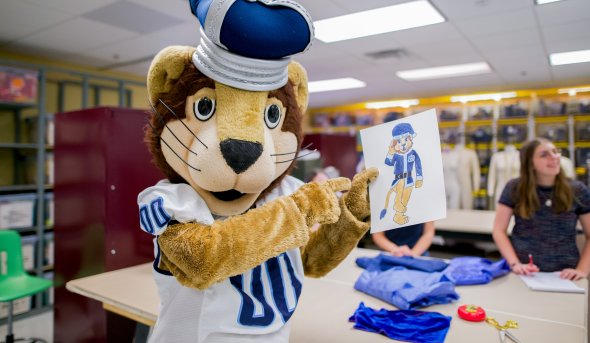 Lion mascot pointing to a drawing of a blue holiday suit