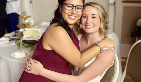 one woman sits on another woman's lap at a wedding 