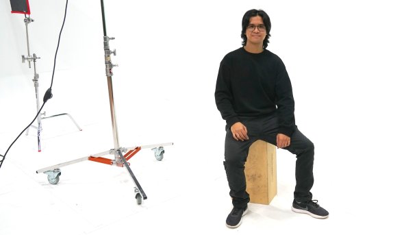 A student sits on a bench in front of a white backdrop.