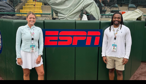 Two people stand in front of a sign that reads "ESPN."