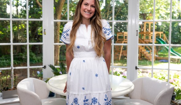 A woman in a white dress leans in a table in a room 