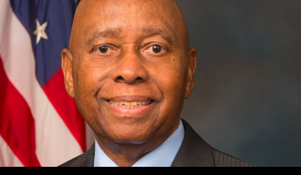 A Black male is posed in front of the American flag. 