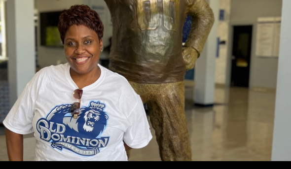 A woman stands in front of a statue of ODU's mascot.