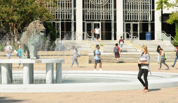 A group of students walk in front of the lion statue and fountain.