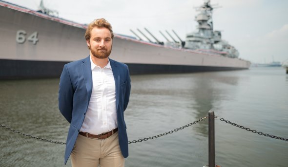 A young man stands on a pier by the Battleship Wisconsin in Nofolk.