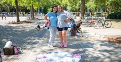 Two students pose for a photo on ODU's campus in front of a crown they painted on the sidewalk. 