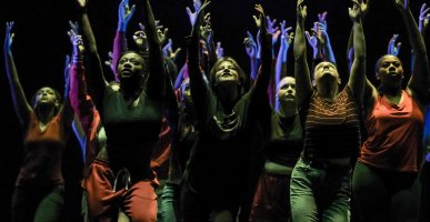 Dancers with lifted hands look upward during performance