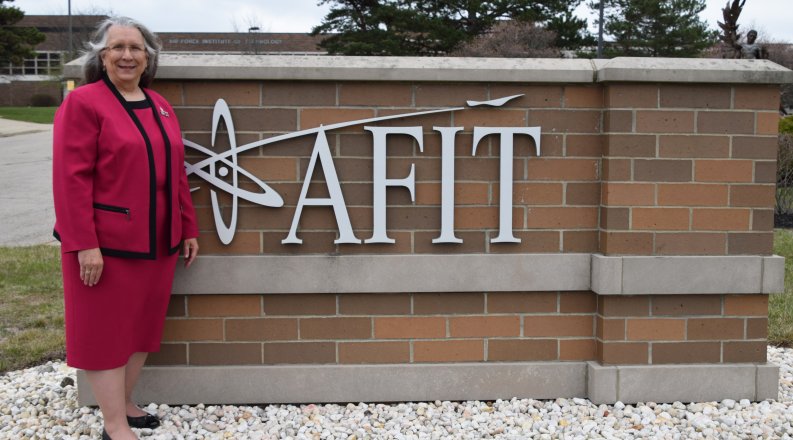 A woman in a red dress stands in front of an outdoor sign 