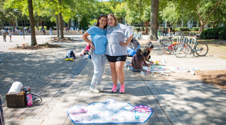 Two students pose for a photo on ODU's campus in front of a crown they painted on the sidewalk. 