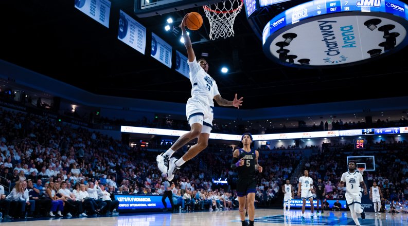 A men's basketball player dunks the ball.