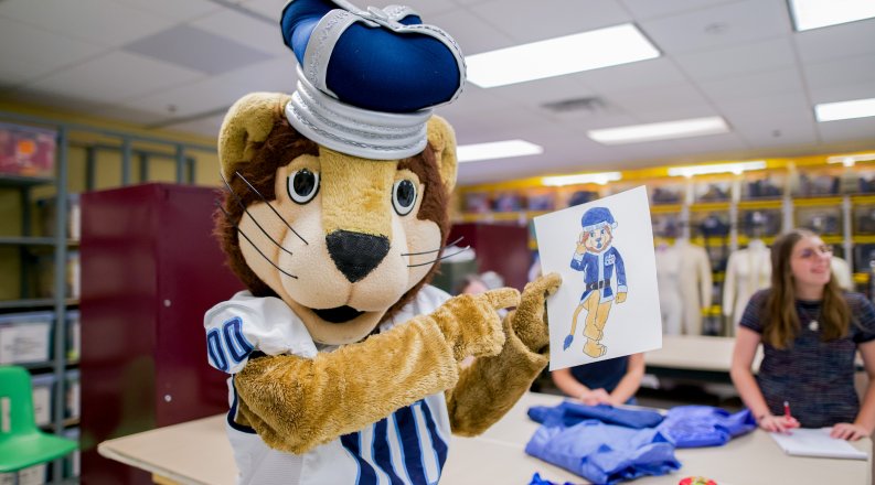 Lion mascot pointing to a drawing of a blue holiday suit