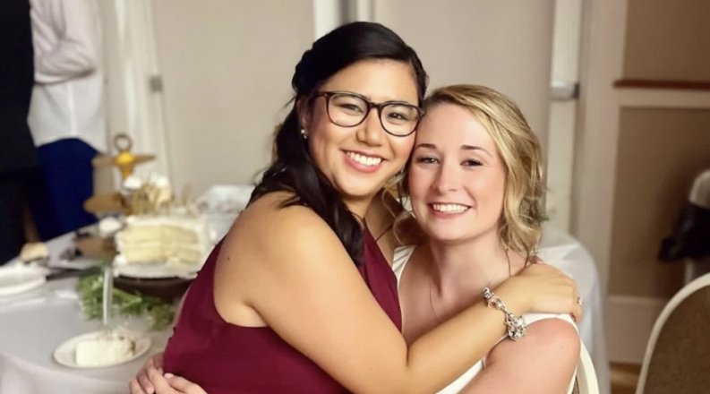 one woman sits on another woman's lap at a wedding 