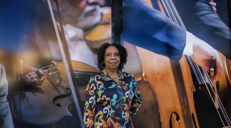 A woman in a patterned blouse stands in front of a mural 