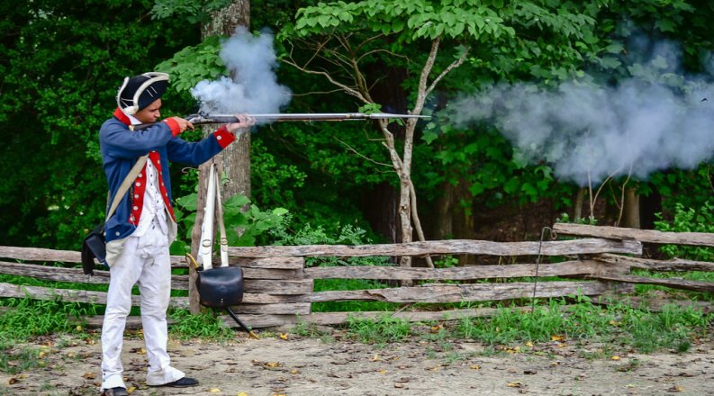ODU student Avery Johnson dressed as an 18th century soldier fires a musket