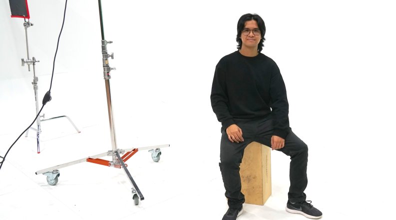 A student sits on a bench in front of a white backdrop.