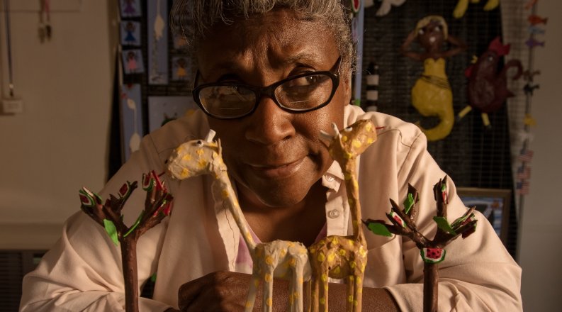 A woman sits behind a set of small animal sculptures.