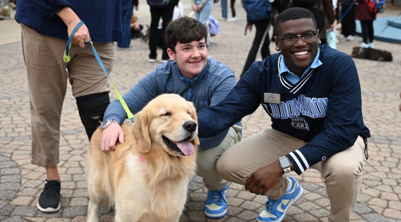 Two men kneel by a service dog.