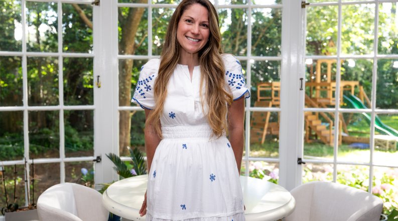 A woman in a white dress leans in a table in a room 