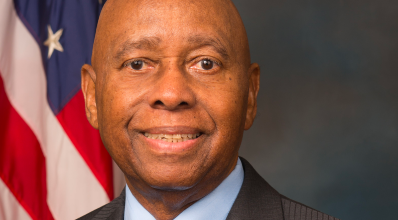 A Black male is posed in front of the American flag. 