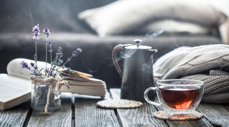 Flowers, tea, a blanket, and an open book on a table.