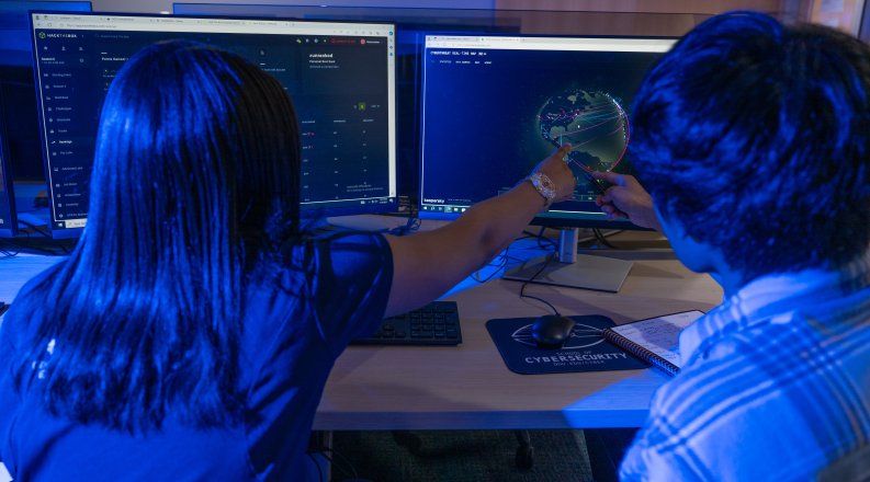 Two students in a computer lab look at an image of a global map.