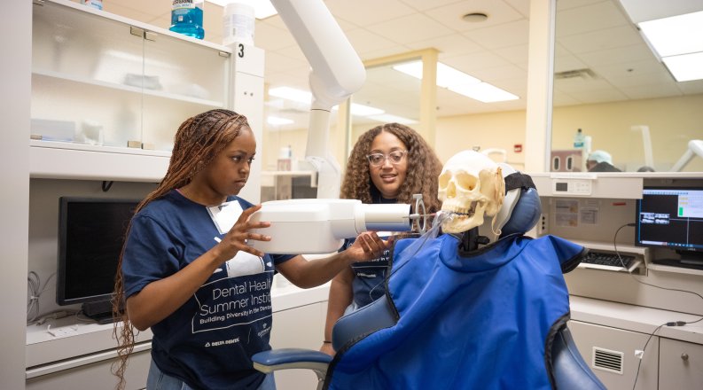 A professor shows a student how to use dental exam equipment.