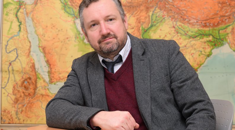 Jared Benton, Ph.D., an ODU associate professor, sits at a table in front of a world map. 