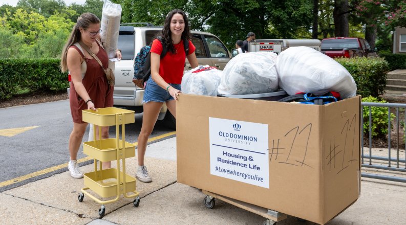 A pair of students push a cart full of items into their dorm.