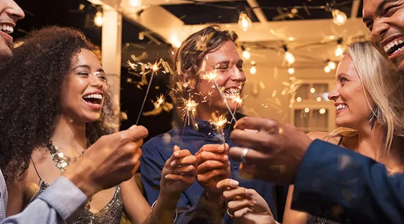 Five friends laugh and smile at a party while holding sparke