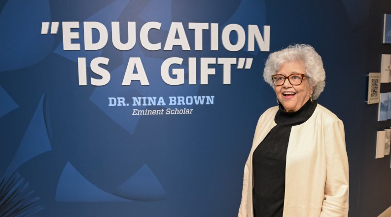 Dr. Nina Brown stands in front of her quote on a wall reading "Education is a gift."