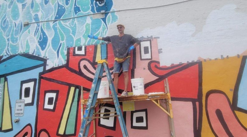 ODU art professor Richard Nickel is pictured standing on scaffolding during the reinstallation of his mural “New Energy of Norfolk.”
