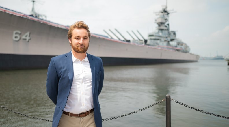 A young man stands on a pier by the Battleship Wisconsin in Nofolk.