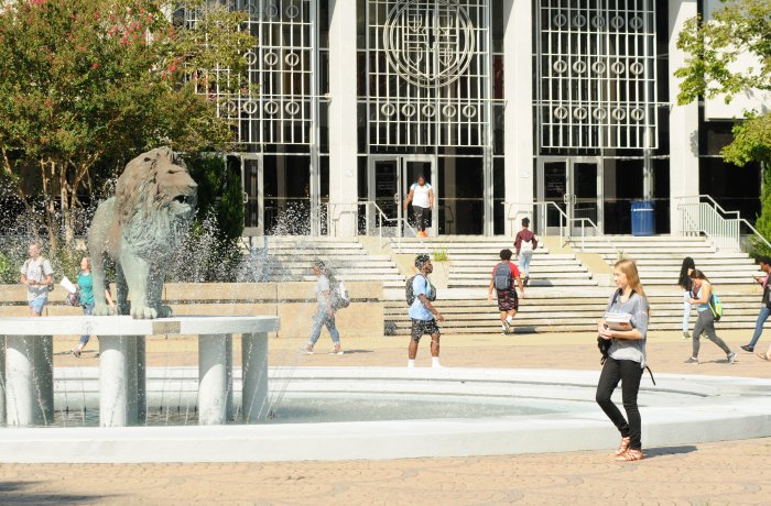 A group of students walk in front of the lion statue and fountain.