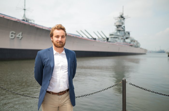 A young man stands on a pier by the Battleship Wisconsin in Nofolk.