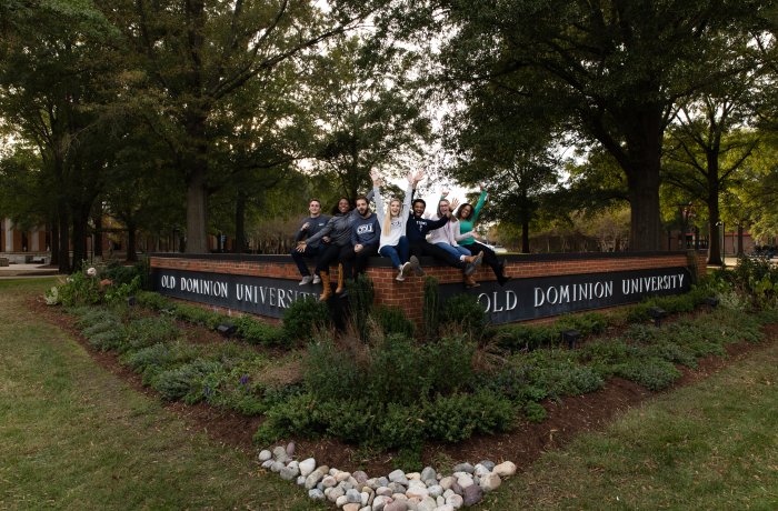 A group of students sit on the Old Dominion University sign.