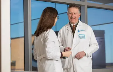 An older male physician speaks with a female resident