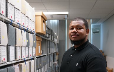 A student stands next to a bookshelf in a library.