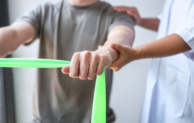 Physical Therapist helps male patient use resistance band