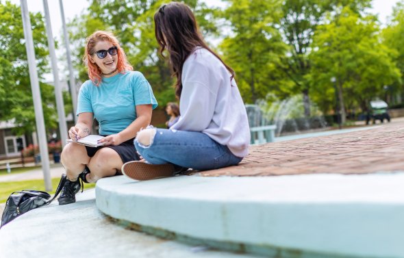 Two female students are sitting on the steps in front of the Webb center talking
