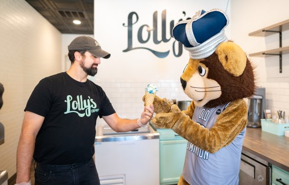 A man hands ice cream to a lion mascot.