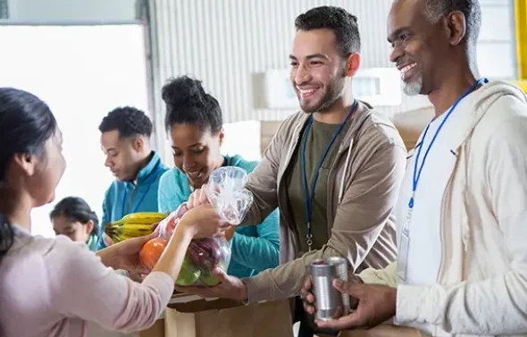 Smiling volunteers fill brown paper bags with fruit for a fo